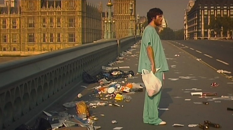 Cillian Murphy as Jim in 28 Days Later, standing in his hospital gowns on Westminster Bridge, which is covered in debris and otherwise completely empty.