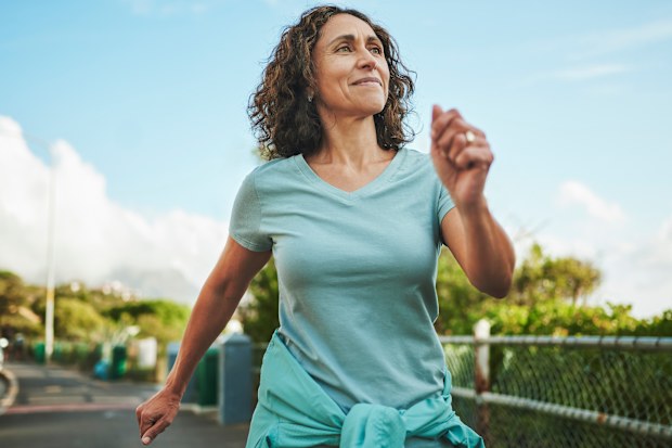 Woman in sportswear smiling while out for a power walk along a sidewalk outside in summer