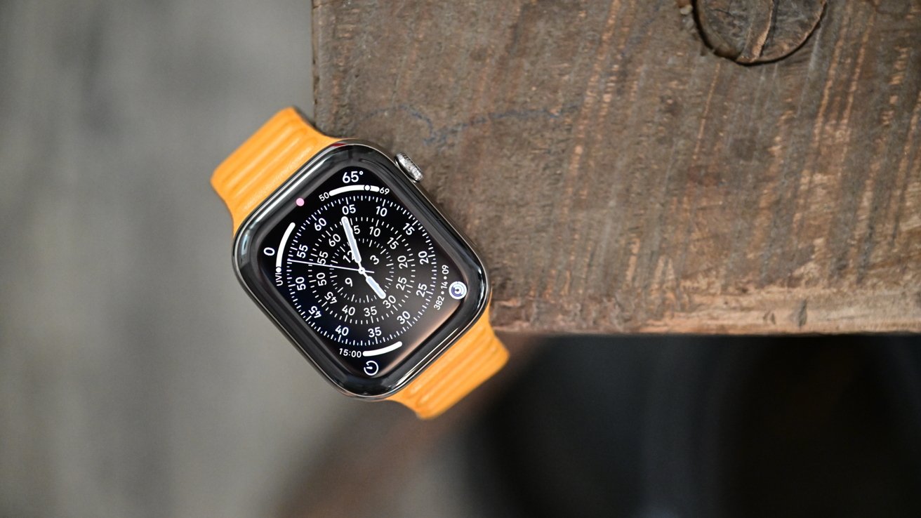 Smartwatch with a detailed black analog-style face and yellow band resting on the corner of a weathered wooden surface