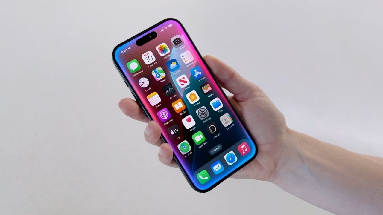 Hand holding a modern smartphone with a colorful screen displaying multiple app icons against a plain light background