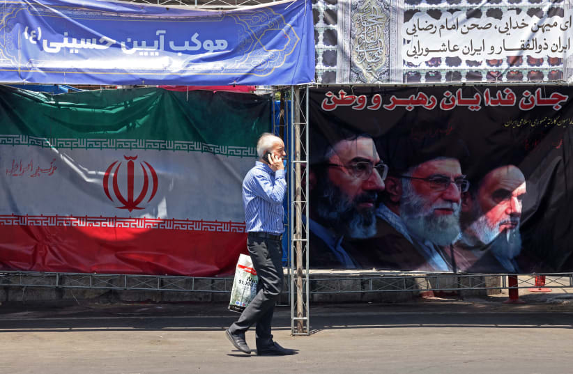 A man walks past Iran’s national flag and a banner bearing the images of the late founder of the Islamic Revolution, supreme leader Ayatollah Ruhollah Khomeini (R), the late Iranian supreme leader Ali Khamenei and his son, the current supreme leader Mojtaba Khamenei (L), in Tehran, June 10.