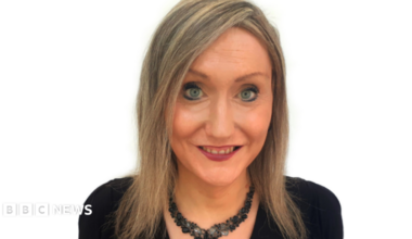 Lisa McNally pictured in front of a white background. She has shoulder length dark blonde hair and is wearing a black necklace and black top.