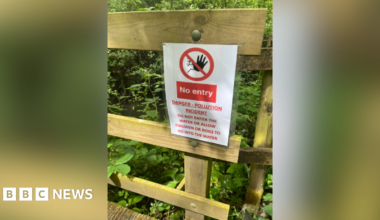 A sign saying 'no entry, danger - pollution incident' warning people not to enter the water. It is attached to a wooden fence.