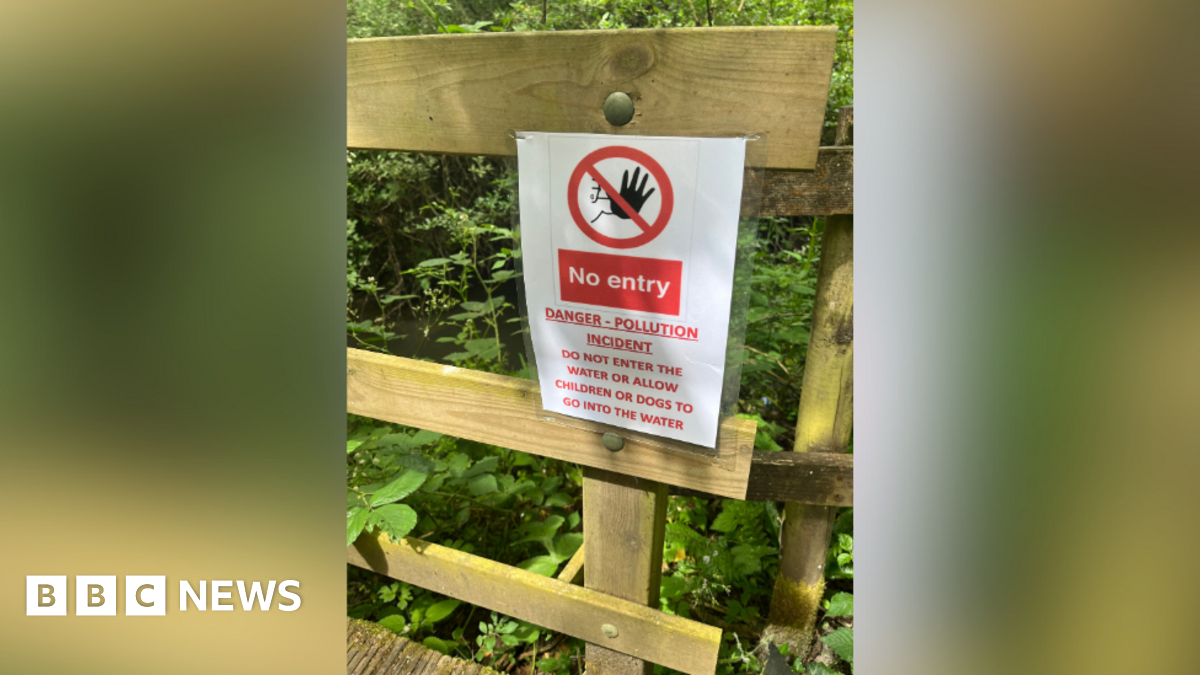 A sign saying 'no entry, danger - pollution incident' warning people not to enter the water. It is attached to a wooden fence.