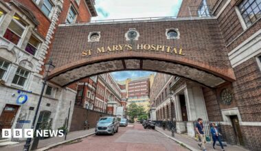 Two brick buildings on either side of a road, with a bridge connecting them. The words 'St Mary's Hospital' appear on gold letters on the bridge.