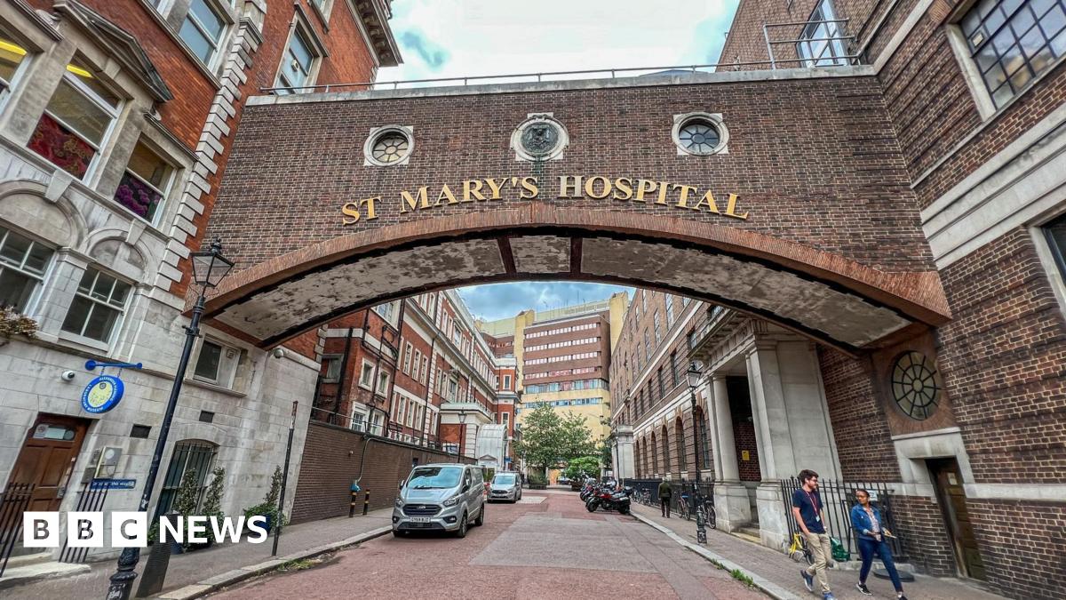 Two brick buildings on either side of a road, with a bridge connecting them. The words 'St Mary's Hospital' appear on gold letters on the bridge.