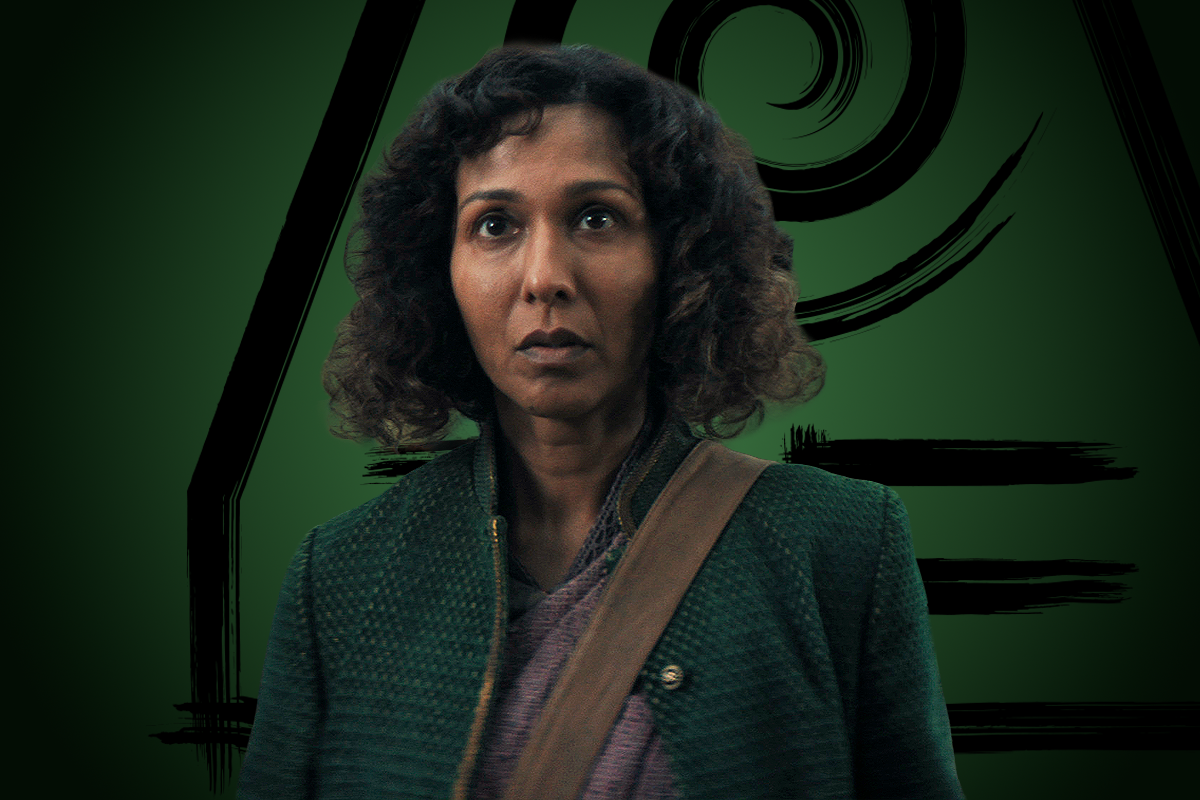 Rekha Sharma as Amita with a serious expression stands against a green background featuring bold, stylized black graphic elements. She wears a textured green coat and a brown shoulder strap, suggesting a purposeful, story-driven setting.