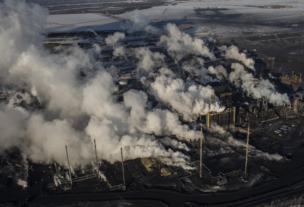 Seen from above, an oil and gas plant in Alberta billows smoke out of smoke stacks.