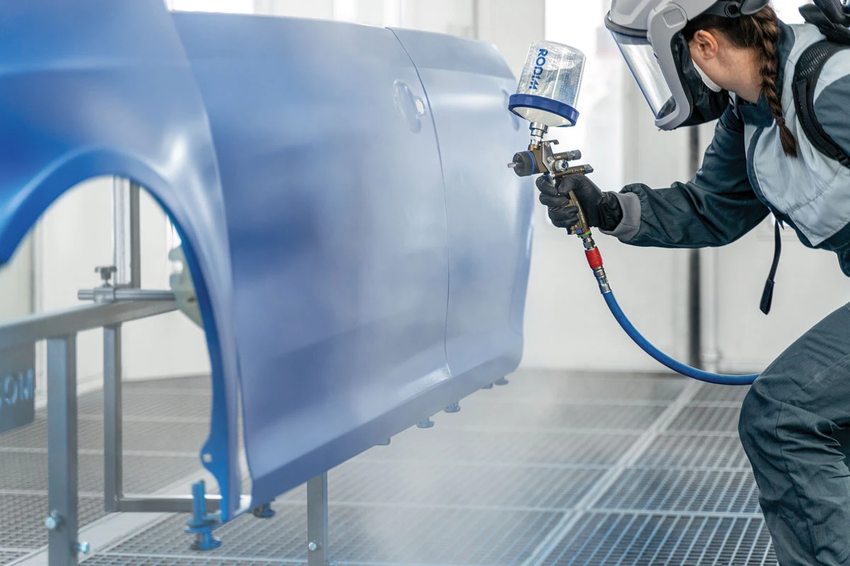 A worker applies an automotive refinish to a vehicle body.