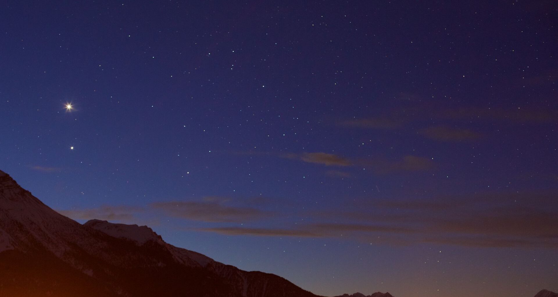 A view of a deep purple night sky with a red glowing mountain range underneath a series of twinkling stars.