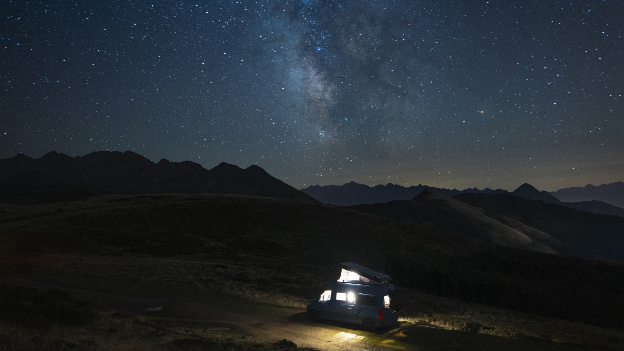 a car with lights on inside under a starry sky with milky way stretching across the center of the image.