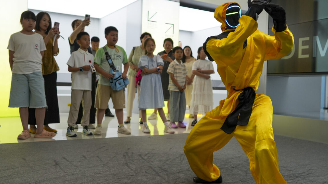 Children watch a martial arts performance by Unitree robots at a humanoid robot store on June 1, 2026 in Zhengzhou, Henan Province of China. The robot is wearing yellow martial arts clothing.
