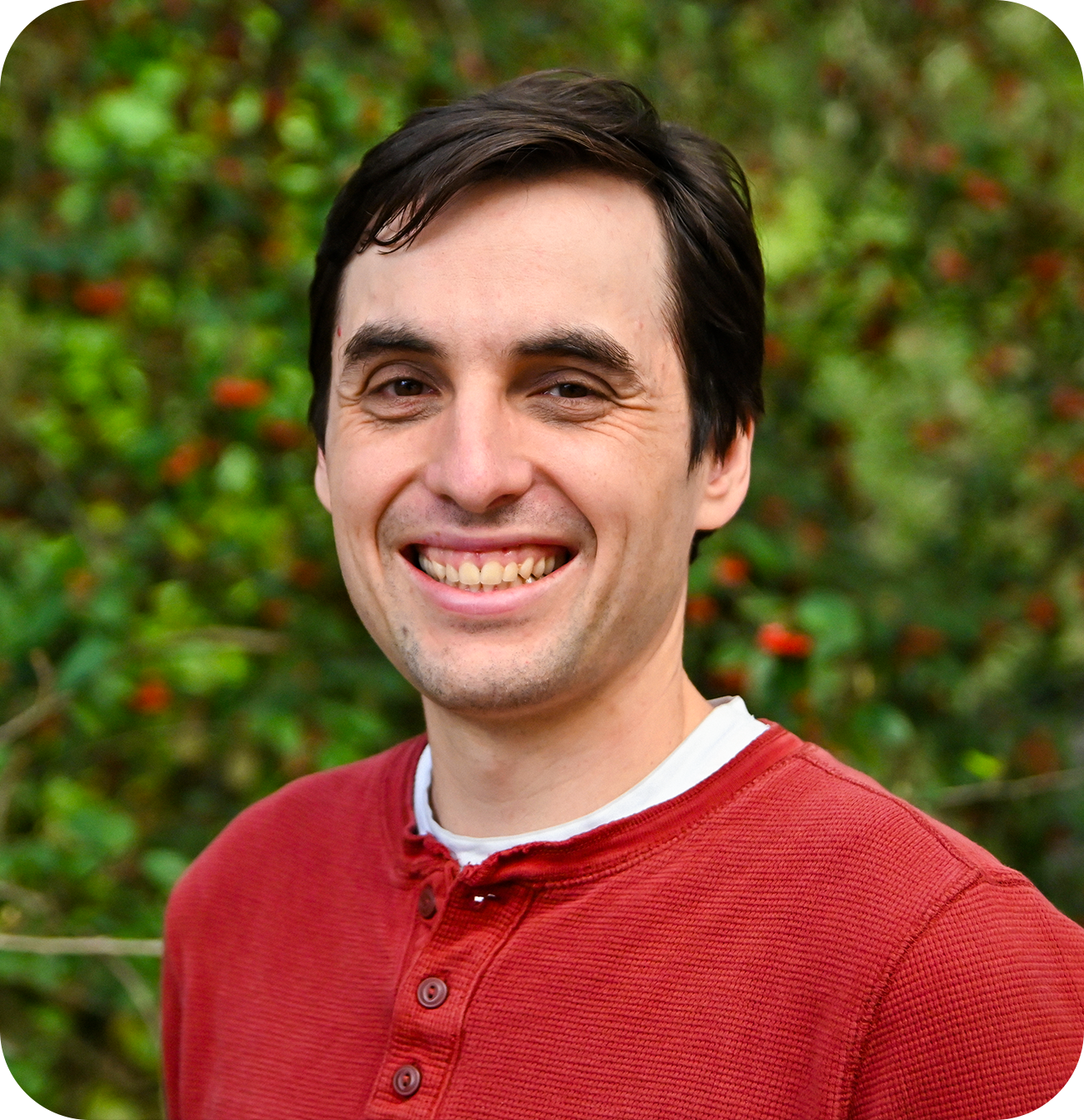 Man in a red shirt photographed in front of plants.