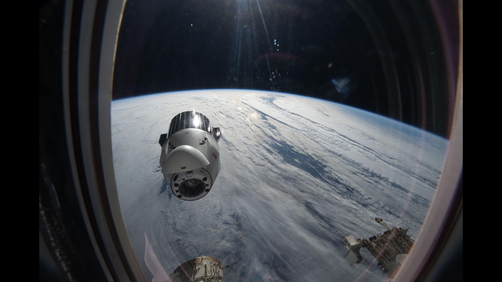A view out of the window of the ISS sees the SpaceX Dragon capsule with Earth in the background.