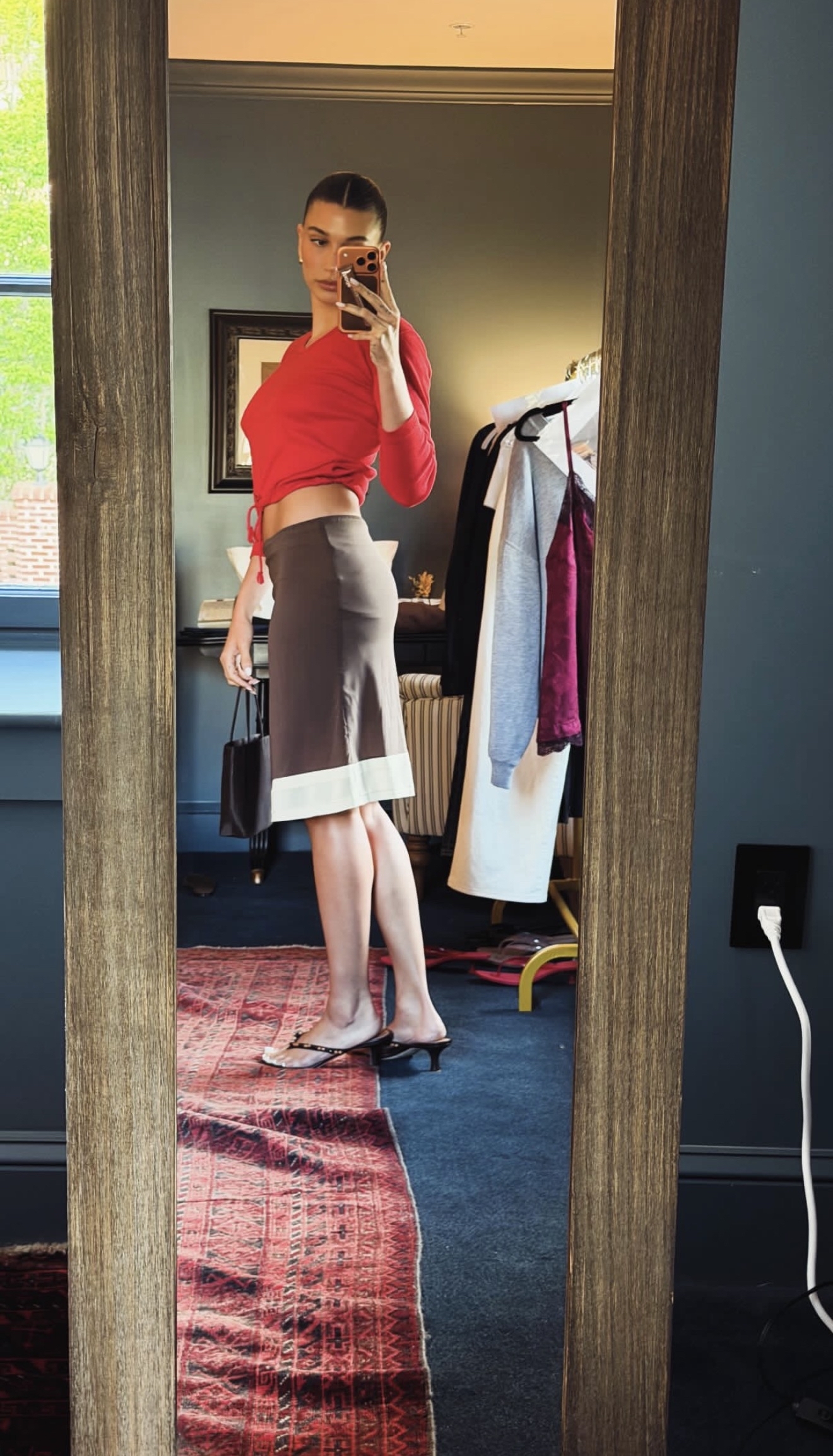 Hailey Bieber at her Rhode Island event wearing a red top and brown skirt with Staud thong sandals.