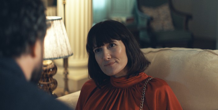 Sarah Solemani image - The Party Sarah Solemani sat back in a chair, wearing a red gown, as she looks up at someone.