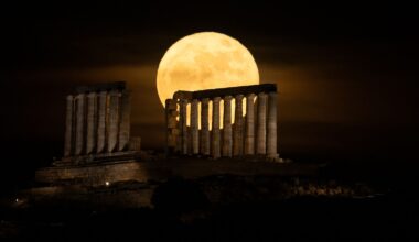 A yellow full moon glows in a dark sky behind the columns of an ancient ruined temple.