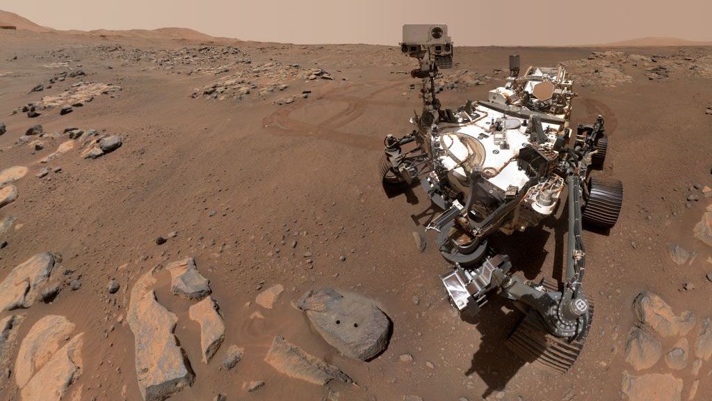 A "selfie" of the Perseverance rover shows a metal/robotic rover on a brownish bit of land with lots of rocks.