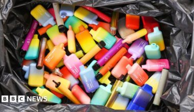 A pile of brightly coloured disposable vape pods fill a black plastic bag.
