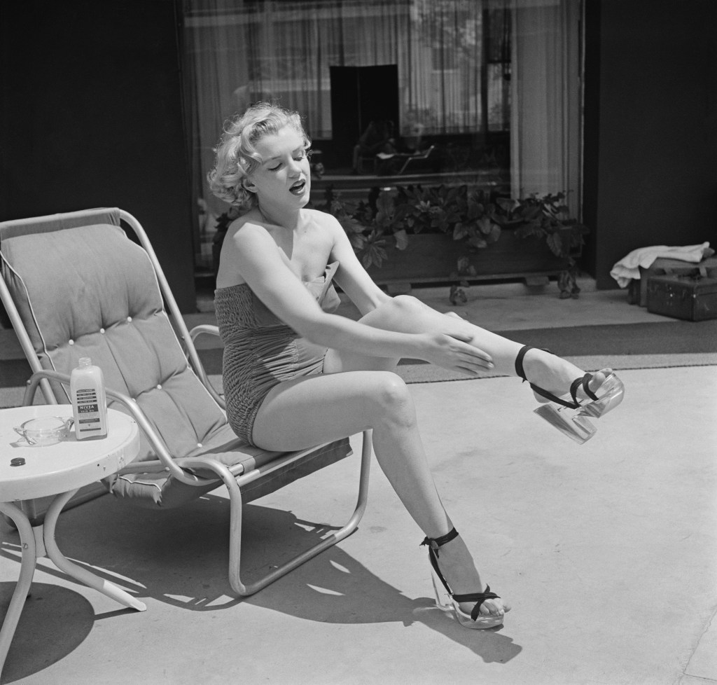 Marilyn Monroe applying Nivea lotion to her legs while sitting in a deckchair.