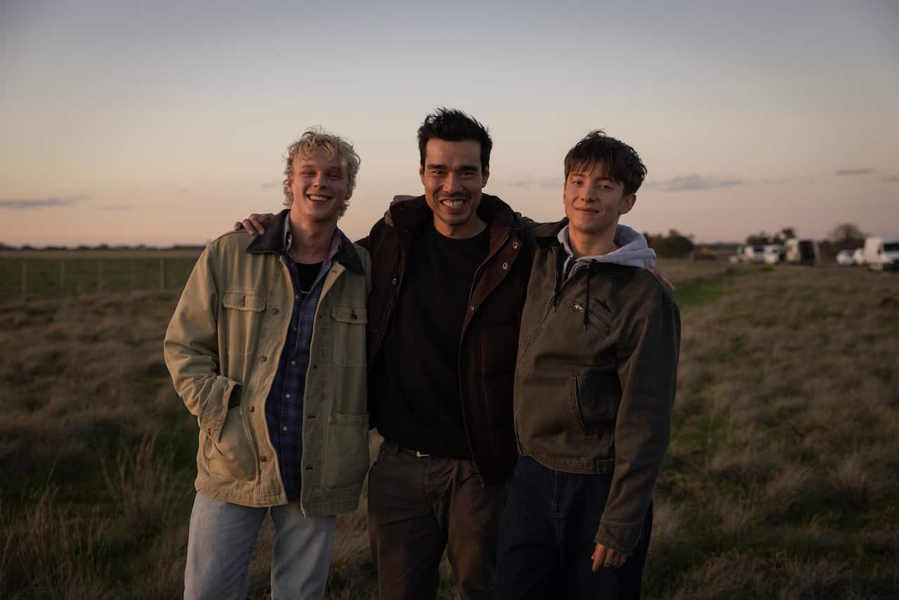 Three men standing together and smiling outside in a paddock