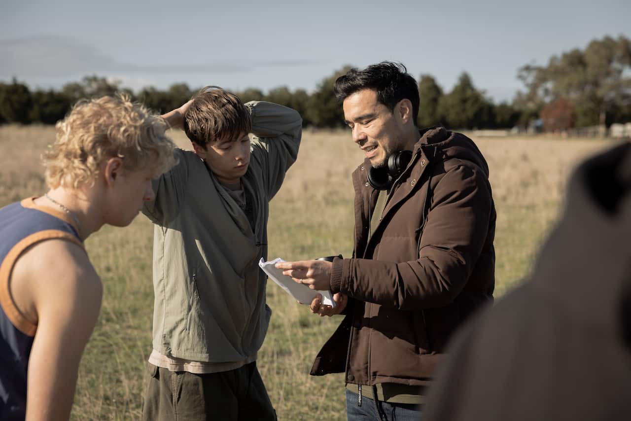 A film director talking with two actors. They're outside in a field.