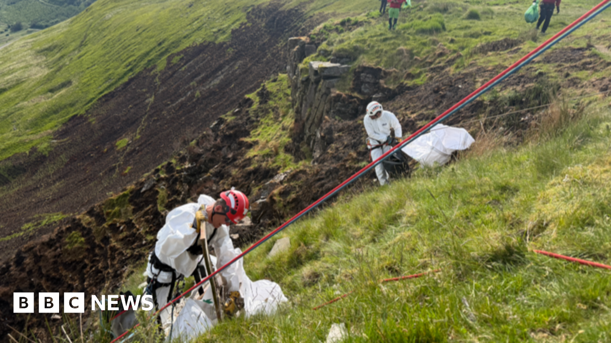 Close up drone image showing people cleaning up piles of rubbish on the side of a mountain. The volunteers are attached to ropes, with crews supporting them on the top of the hill.