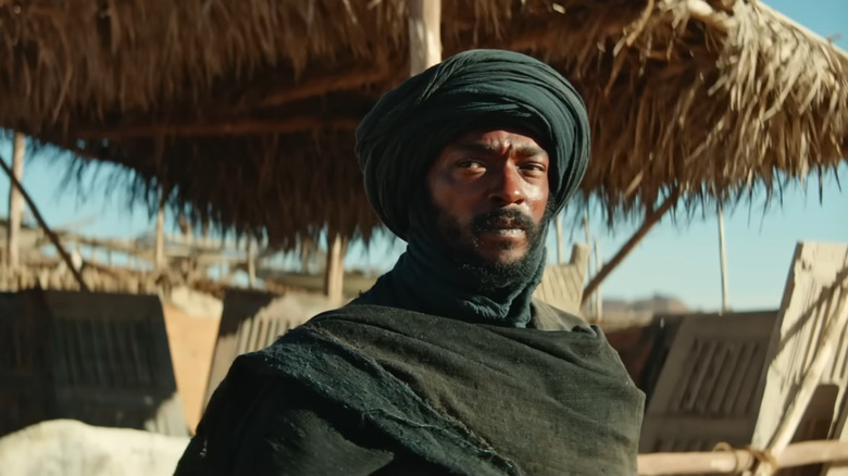 Anthony Mackie as the bandit standing in front of a grass hut in Desert Warrior