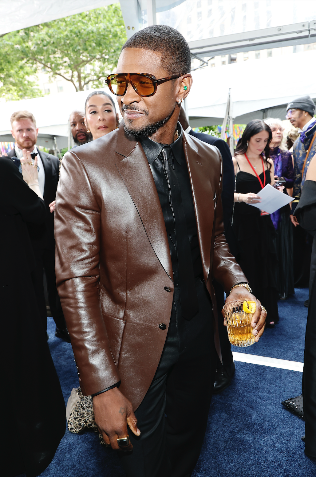 Man in brown leather jacket holding a drink at a formal event.