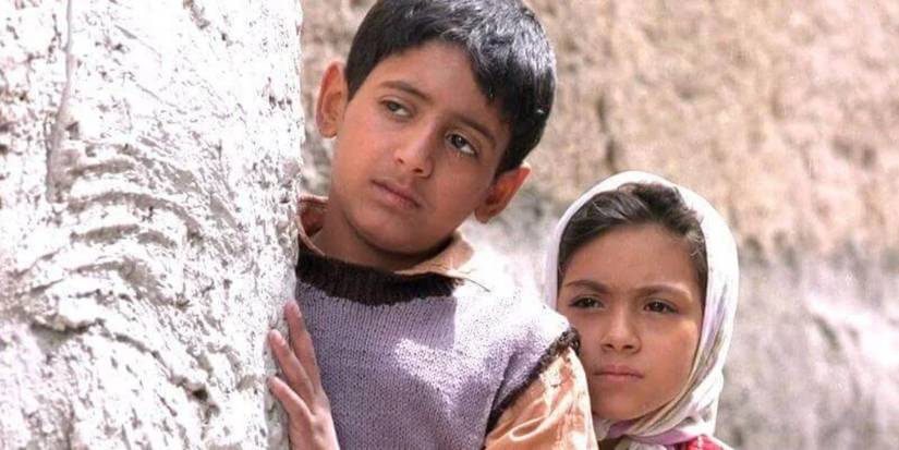 Two children looking from behind a wall in Children of Heaven