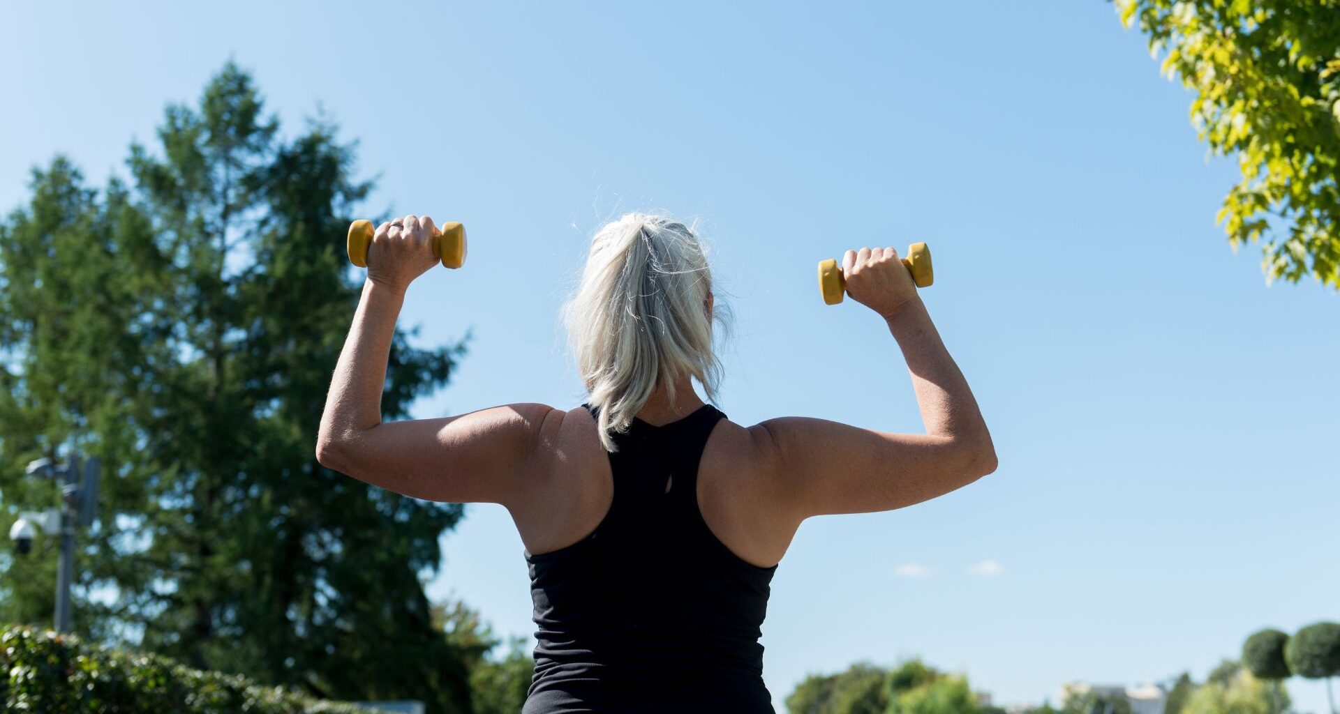woman with dumbbells in shoulder press overhead looking at the sky
