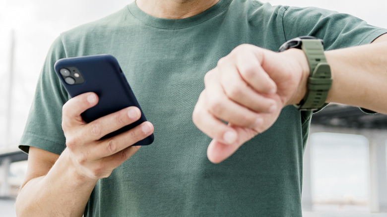 A close up of a man holding a phone in one hand, wearing a smartwatch on the other wrist