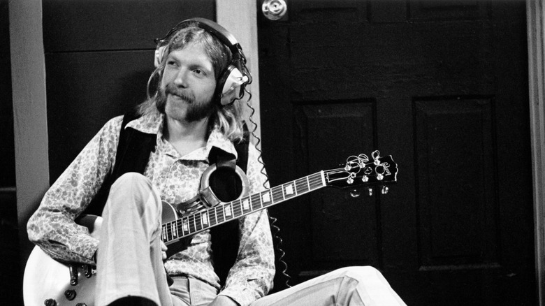 Duane Allman seated on ground with guitar and headphones