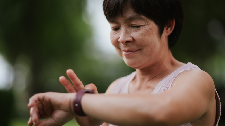 An individual with black hair and wearing a soft pink tank top has their right index finger on their smart watch