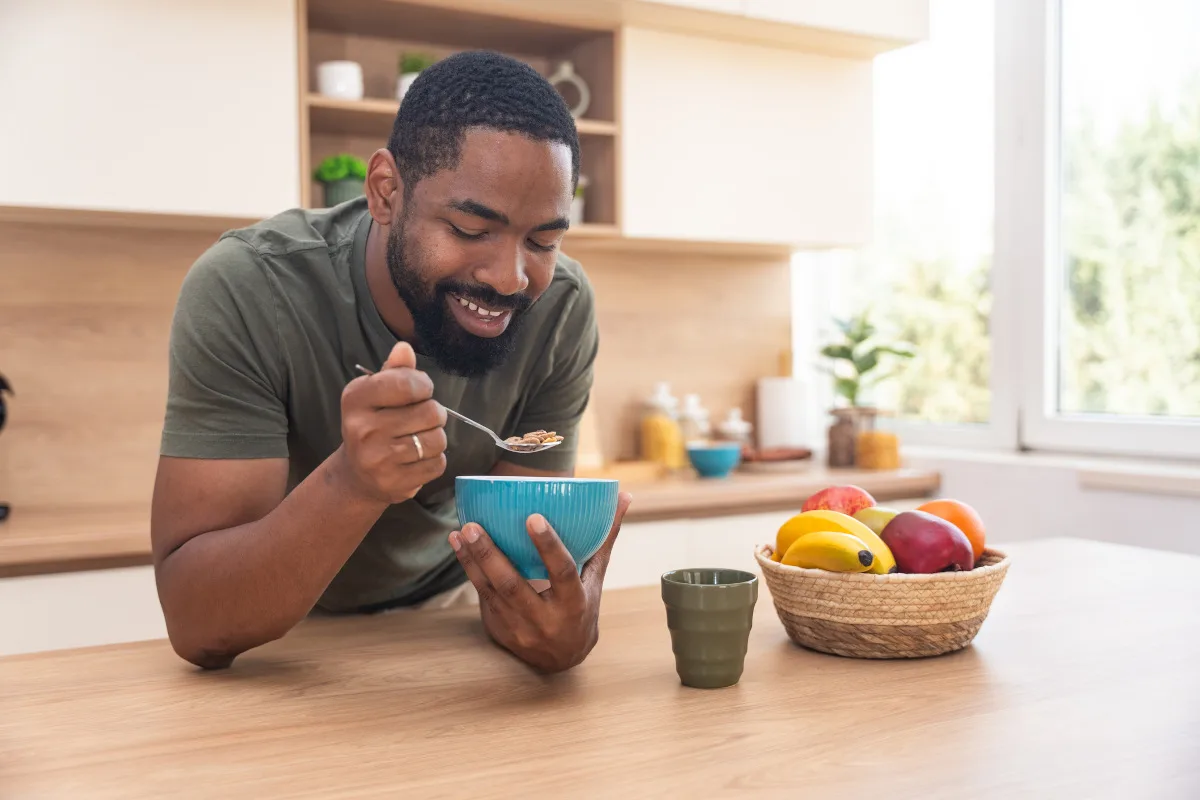 Photo of a smiling man eating breakfast from a bowl in their kitchen