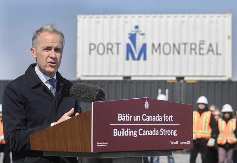 an older man in a dark suit speaks at a podium