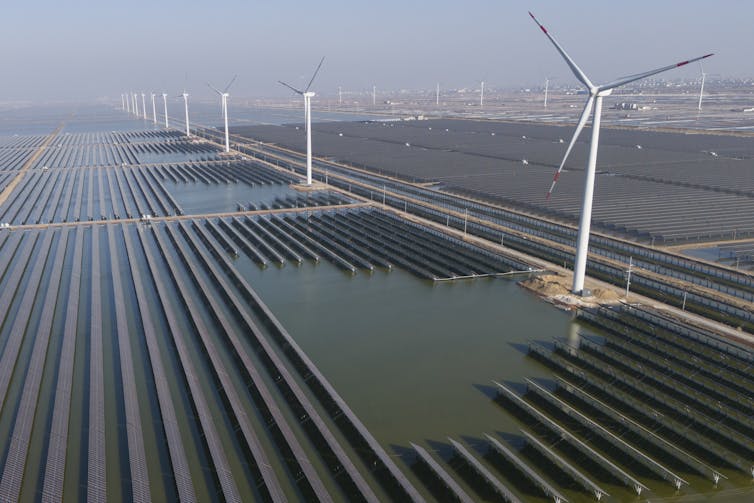 a massive solar panel farm with a row of wind turbines stretching into the distance