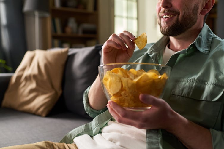 A young man sitting on a sofa with a bowl of crisps