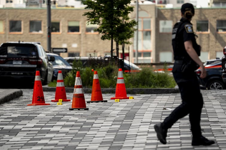 A police woman walks past a segment of pavement with red pilons around it.