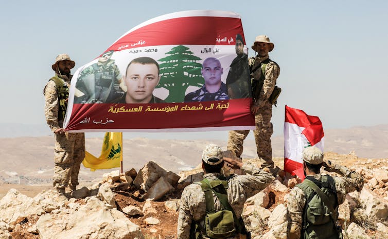 Men in fatigues salute a large banner.