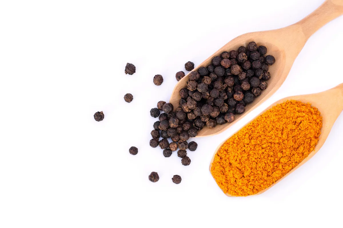 Turmeric and black pepper in wooden spoons isolated on white background