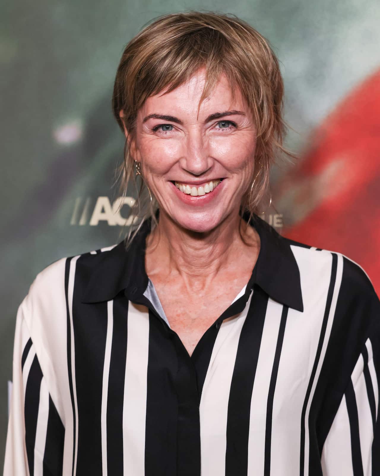 A woman wearing a striped shirt smiling in front of a media wall.