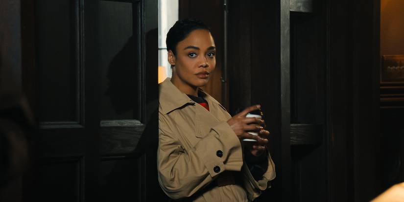 Tessa Thompson in a trench coat standing in a doorway in His & Hers.