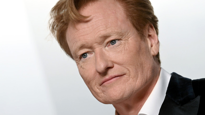 Photo showing a close-up of comedian Conan O'Brien. He's wearing a suit and standing in front of a white backdrop.