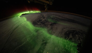 The aurora looks like a long, curving line of green mist arcing over Earth. Our home planet is dark, blending into the blackness of space on the right side of the image.