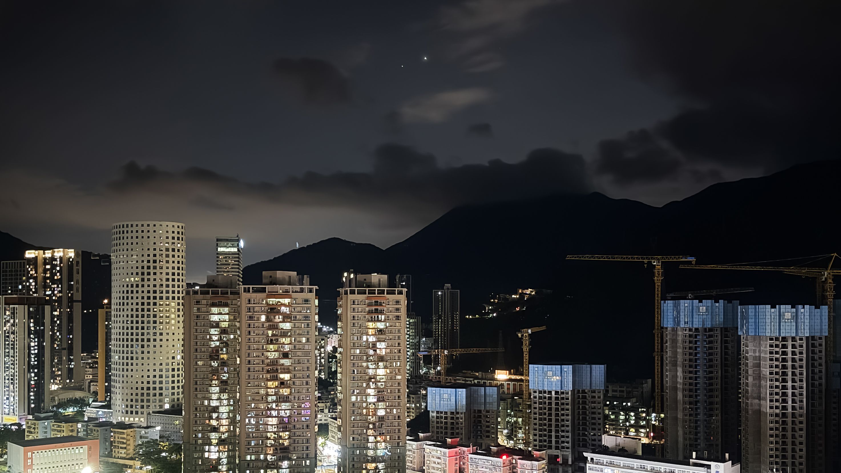 Two star-like planets glow close to one another in the night sky above a city skyline