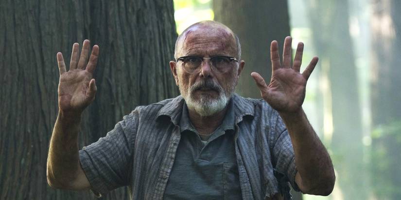 Joe Pantoliano raising his hands in surrender in the woods in Last of Us