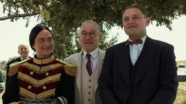 Ernest Burkhart (Leonardo DiCaprio) and Mollie Burkhart (Lily Gladstone) stand with William Hale (Robert De Niro) after being married in Killers of the Flower Moon