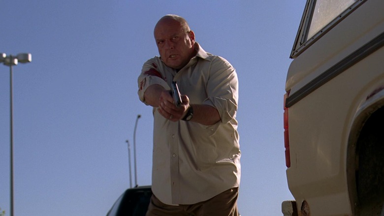 Dean Norris as Hank holding a gun behind a car in Breaking Bad