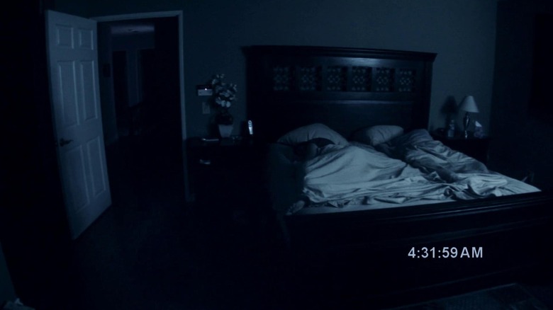 Katie Featherston as Katie and Micah Sloat as Micah in Paranormal Activity, sleeping in bed as the camera observes their dark bedroom.